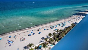 A beach with numerous umbrellas and people, a clear blue sea, and a distant ship. - Beachfront Luxe Corner Penthouse|Gym|Heated Pool (Hollywood)