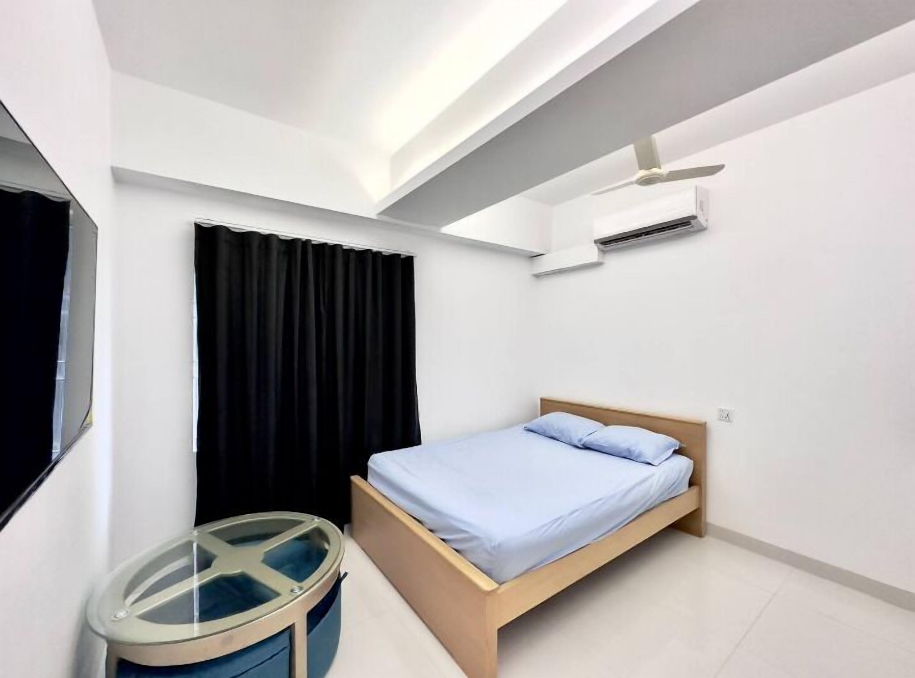 A bedroom with a bed, a small round table, a window with black curtains, and an air conditioning unit on the wall.