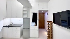 Une cuisine compacte avec des meubles blancs, un réfrigérateur, un évier et un téléviseur encastré.