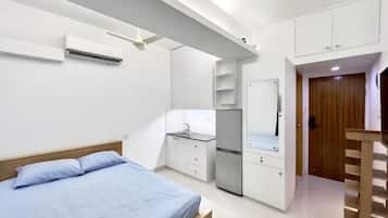 Une chambre comprenant un lit, une petite kitchenette, une armoire et une porte donnant sur une autre pièce.
