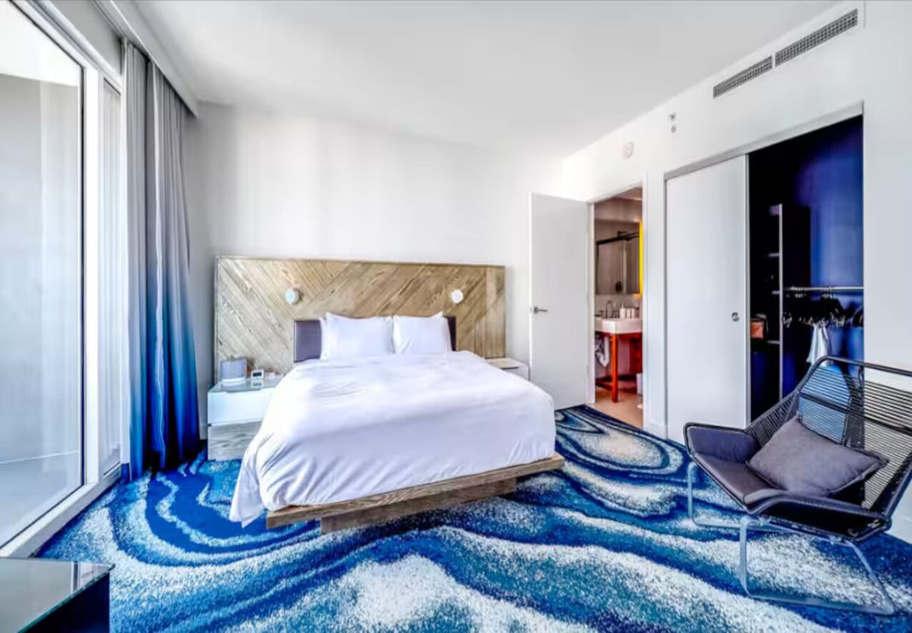 Una habitación de hotel moderna con una cama grande, un área de descanso con una silla y vistas al baño y la cocina.