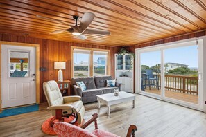 A spacious living room with a ceiling fan, a sofa, a coffee table, and a view through large sliding glass doors to an outdoor deck.
