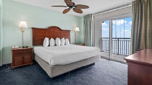 A hotel room with a large bed, a wooden headboard, two bedside lamps, a nightstand, a desk, and a balcony with a view.