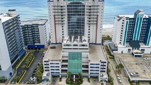 A high-rise hotel with a central glass facade, multiple floors, and a parking area in front.