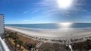 A beach view from a hotel balcony with a swimming pool and a boardwalk.