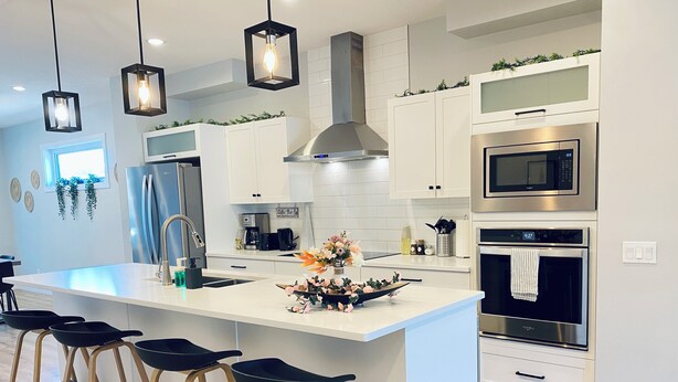 A modern kitchen with white cabinetry, a large island with bar stools, stainless steel appliances, and pendant lighting.