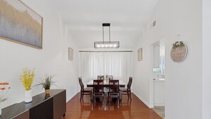 A dining area with a wooden table and chairs, a modern pendant light, and a white wall with a framed picture. - Stripside Serenity –  4B3B Family Retreat, 5 mins from the strip (Las Vegas)