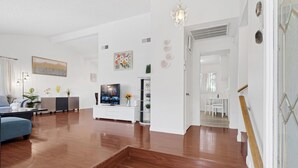 A spacious living room with a wooden floor, a TV, a white entertainment unit, and a staircase leading to another room. - Stripside Serenity –  4B3B Family Retreat, 5 mins from the strip (Las Vegas)
