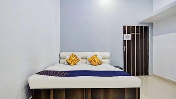 A bedroom with a bed, two pillows, a bedside table, and a door.