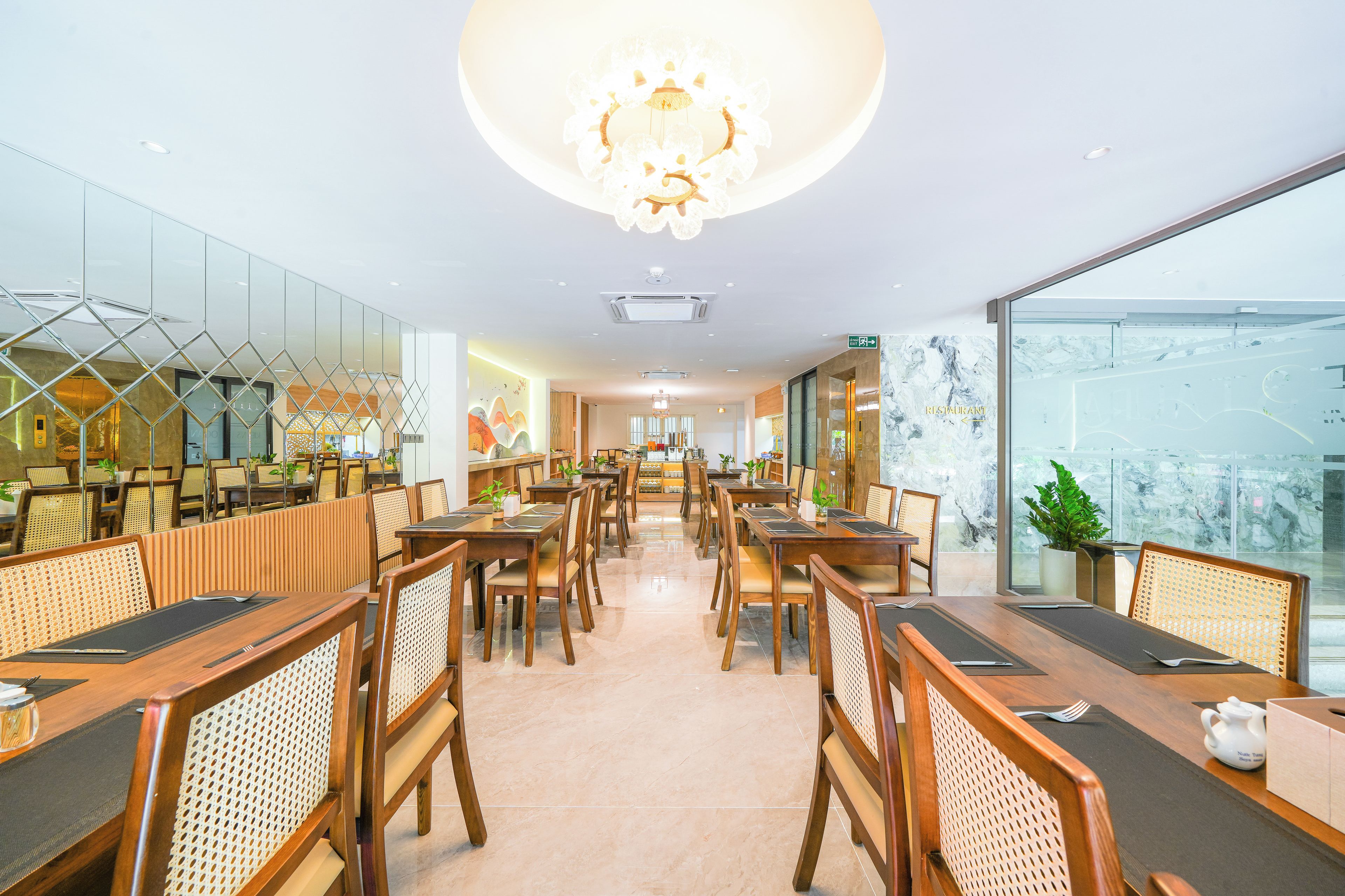A modern dining area with wooden tables and chairs, a central chandelier, and large windows offering a view of the city.