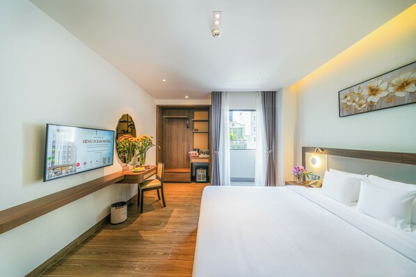 A hotel room with a bed, a desk with a chair, a television, and a view of the outside. - Kien Ocean Hotel (Da Nang Municipality)