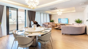 Moderni hotellihuone, jossa on ruokailutila, oleskelutila ja suuri ikkuna, jossa on verhot.