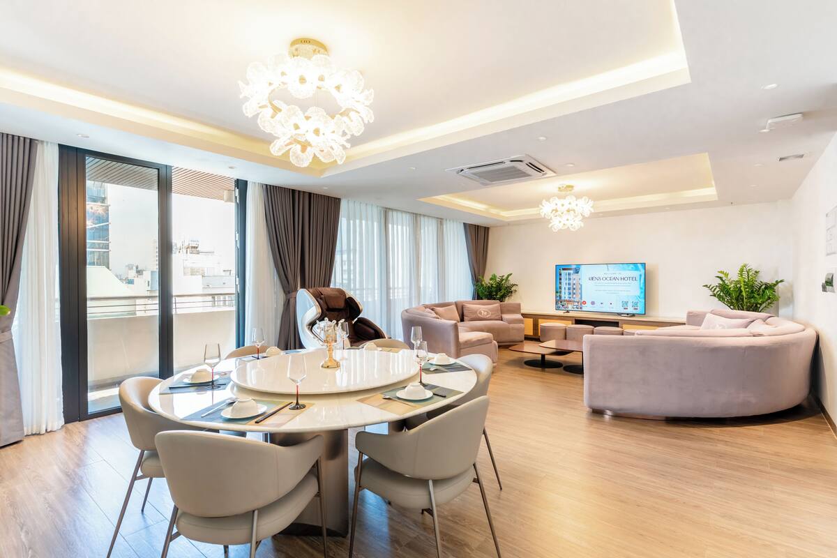 Ett modernt hotellrum med en matplats, ett vardagsrum och ett stort fönster med gardiner.