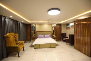 Habitació d'hotel amb un llit gran, una zona de seients amb una cadira, un armari i un mirall.