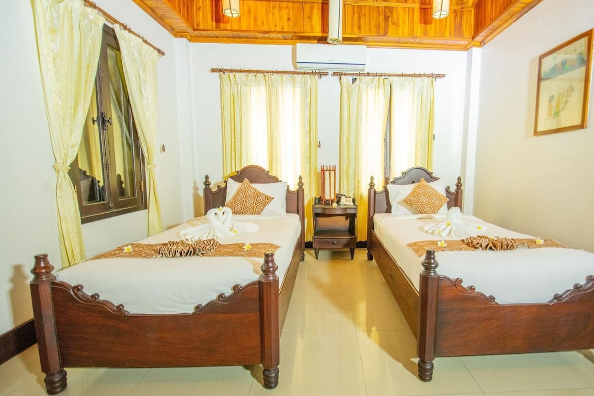 A hotel room with two wooden beds, a wooden ceiling, and a small table between the beds.
