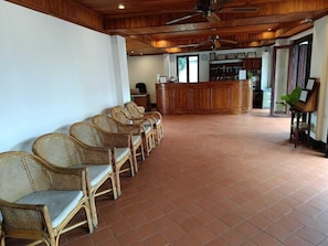 A reception area with a wooden reception desk, wicker chairs, and a tiled floor.