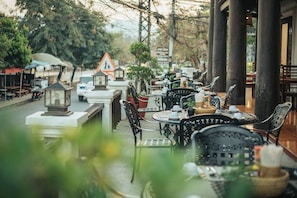 An outdoor cafe with tables and chairs, surrounded by trees and buildings.