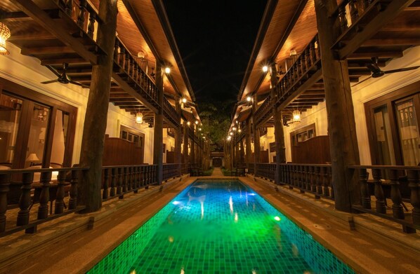 A pool area with a central water feature, flanked by wooden buildings with balconies and lights.