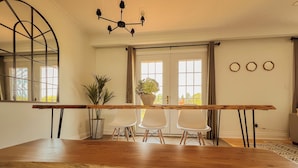 A dining area with a long wooden table, two white chairs, a potted plant, and a chandelier. - Beautiful Waterfront Cottage with Pool & HomeTheater (Georgina)