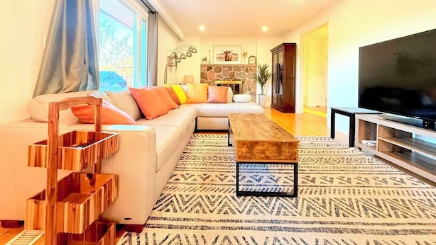 A modern living room with a sofa, coffee table, TV, and patterned rug. - Beautiful Waterfront Cottage with Pool & HomeTheater (Georgina)