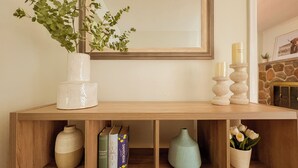 A wooden console table with a mirror above it, a vase with green foliage, and books on the shelf. - Beautiful Waterfront Cottage with Pool & HomeTheater (Georgina)