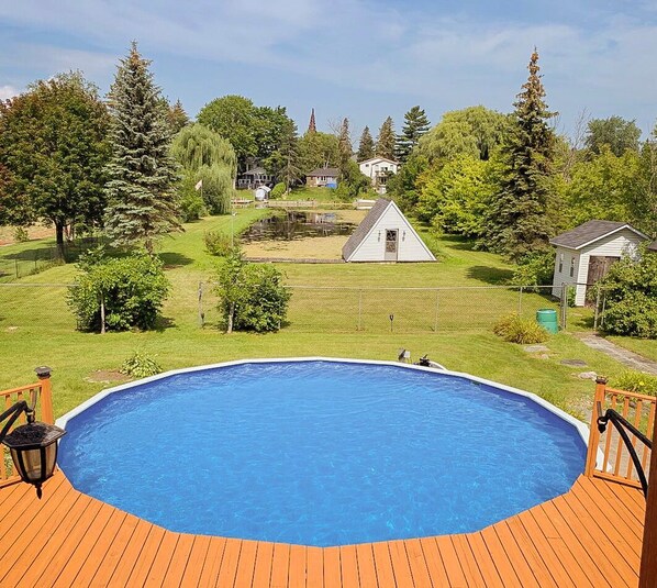 A swimming pool on a wooden deck with a view of a residential area and a small house in the background.