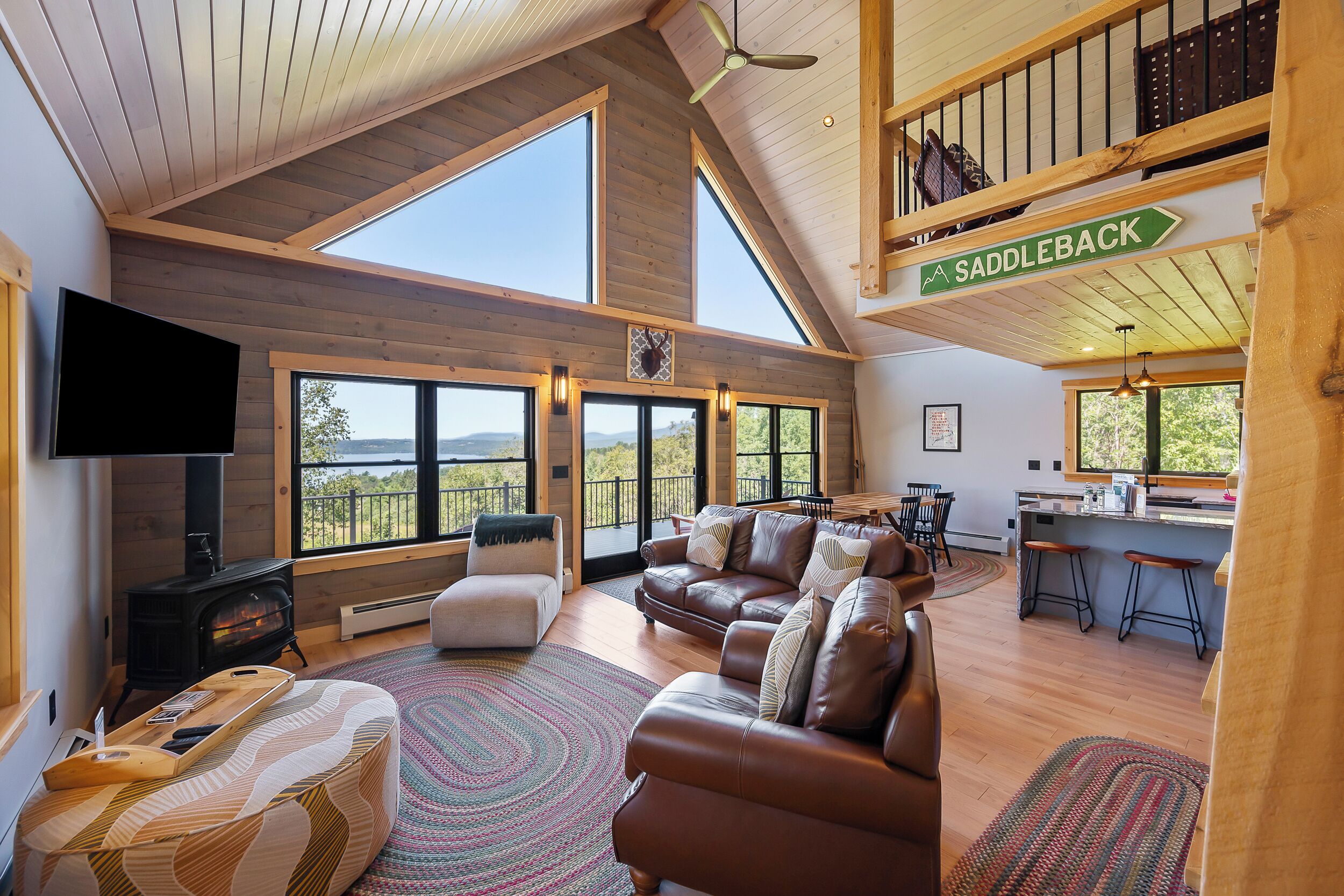 Amplia sala de estar con chimenea, sofá de cuero y ventanas grandes que ofrecen vistas al exterior.