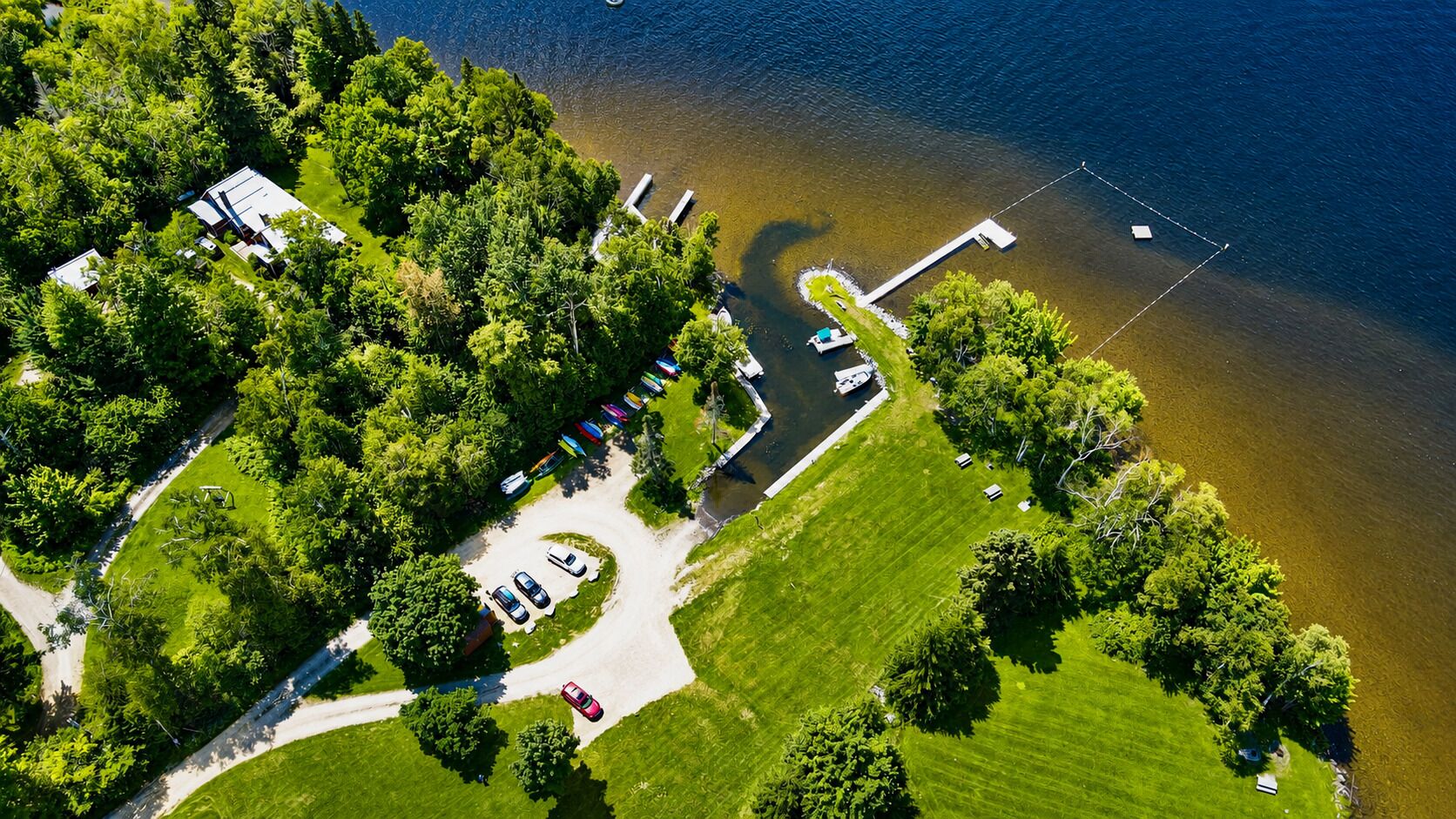 Vista aérea de una propiedad junto al lago con muelle, zona de estacionamiento y exuberante vegetación.