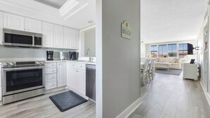 A modern kitchen with white cabinets, stainless steel appliances, and a black mat. - Light bright airy loggerhead cay unit 314 New! (Sanibel)