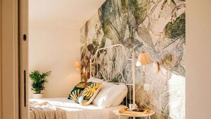 Une chambre à coucher avec un lit, une table de chevet, une lampe, une fresque murale et une plante en pot.