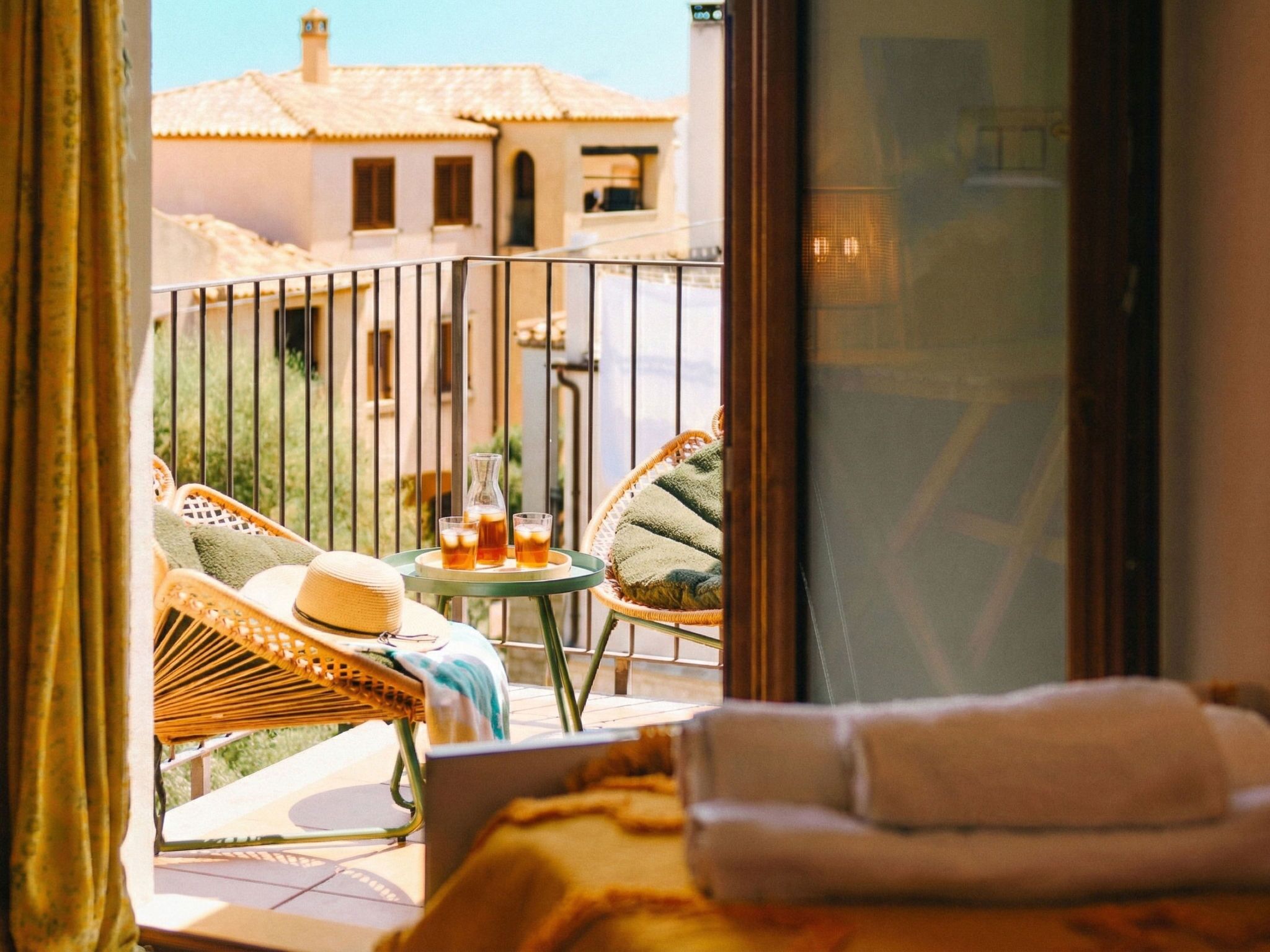 A balcony with wicker furniture, a small table with drinks, and a view of buildings in the background.