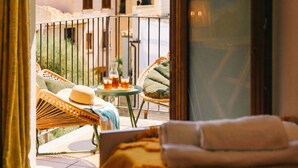 Un balcon agrémenté de meubles en osier, une petite table avec des boissons, et une vue sur les bâtiments en arrière-plan.