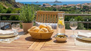 A table set with bread, olives, a glass of water, and a bottle of lemonade, overlooking a scenic coastal view. - La Meravigliosa Sardegna by Interhome (Santa Maria Navarrese)