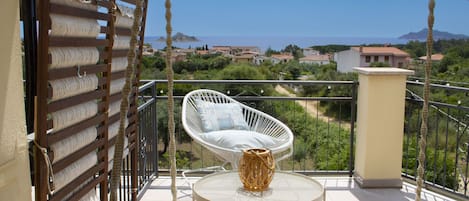 A balcony with a white wicker chair, a small round table, and a rope barrier.