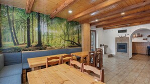 Un restaurant chaleureux avec des tables et des bancs en bois, une fresque représentant une forêt sur le mur et une cheminée.