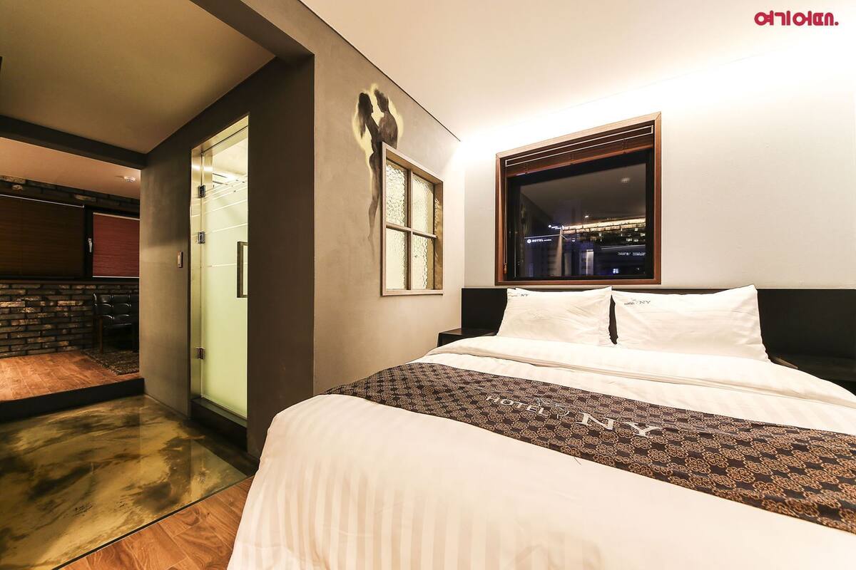 Ein Hotelzimmer mit Bett, Fenster mit Stadtblick, einer Tür und einem Wandbild.