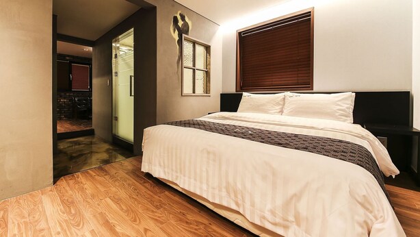 A bedroom with a bed, a window with blinds, a wall-mounted artwork, and a wooden floor. - Yeongdeungpo Station New York Hotel (Seoul)