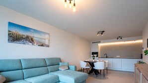 A modern living room with a teal sofa, a round coffee table, and a dining area with a white table and chairs. - Elyana with balcony by Interhome (Blankenberge)