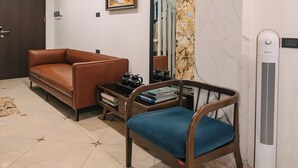 Eine Lobby mit einem braunen Sofa, einem blauen Sessel, einer Uhr, einem gerahmten Bild, einer Marmorwand und einem Standventilator.