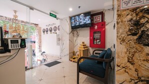 Ein Hotel-Empfangsbereich mit Marmorboden, einem an der Wand montierten Fernseher, einer Brandschläucheinrichtung und einem Stuhl mit Kissen.