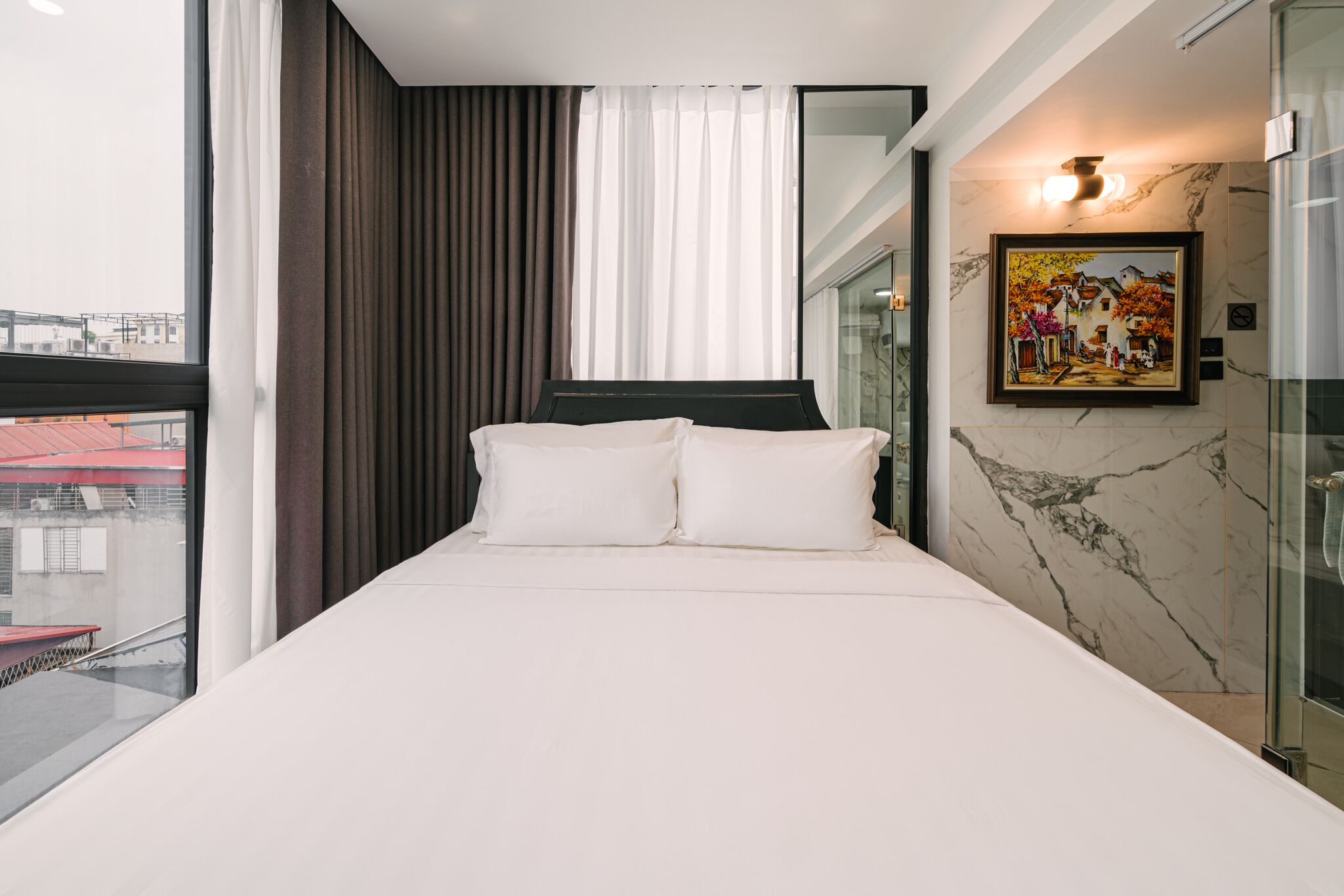 A modern hotel room with a large bed, a painting on the wall, and a view of the city through the window.