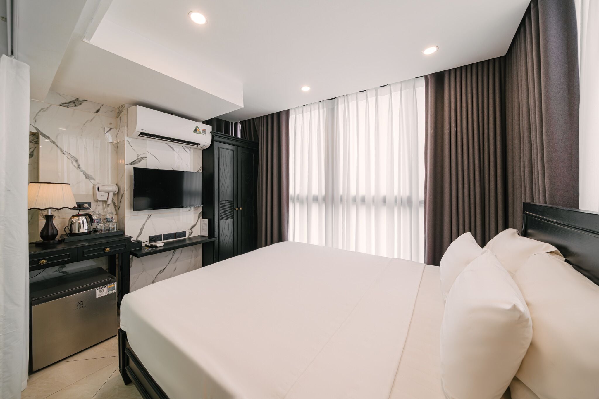 A hotel room with a bed, a desk with a flat-screen TV, an air conditioner, and a minibar.