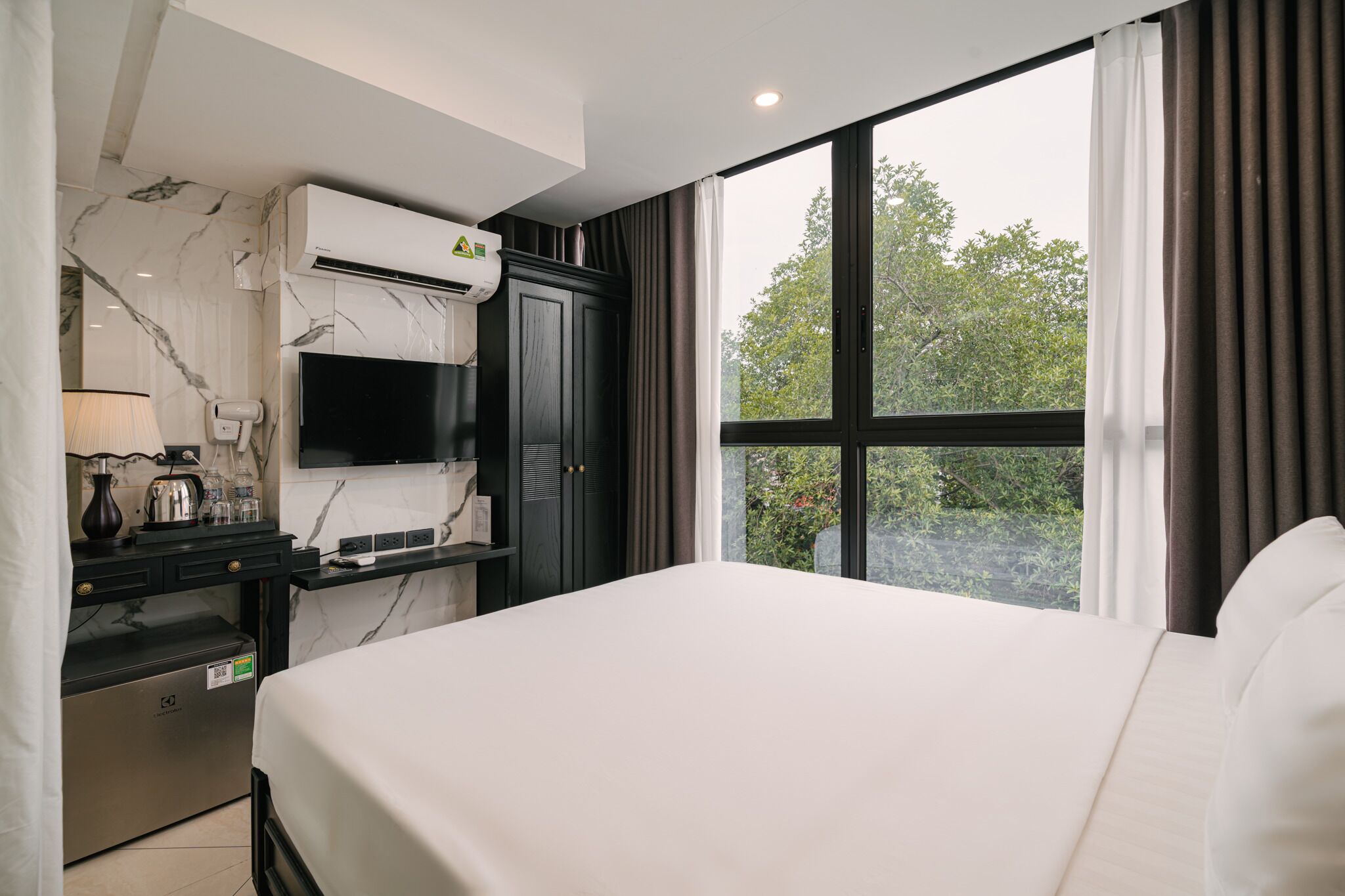 Habitación de hotel con cama, escritorio, televisor de pantalla plana, secador de pelo y ventana con cortinas.