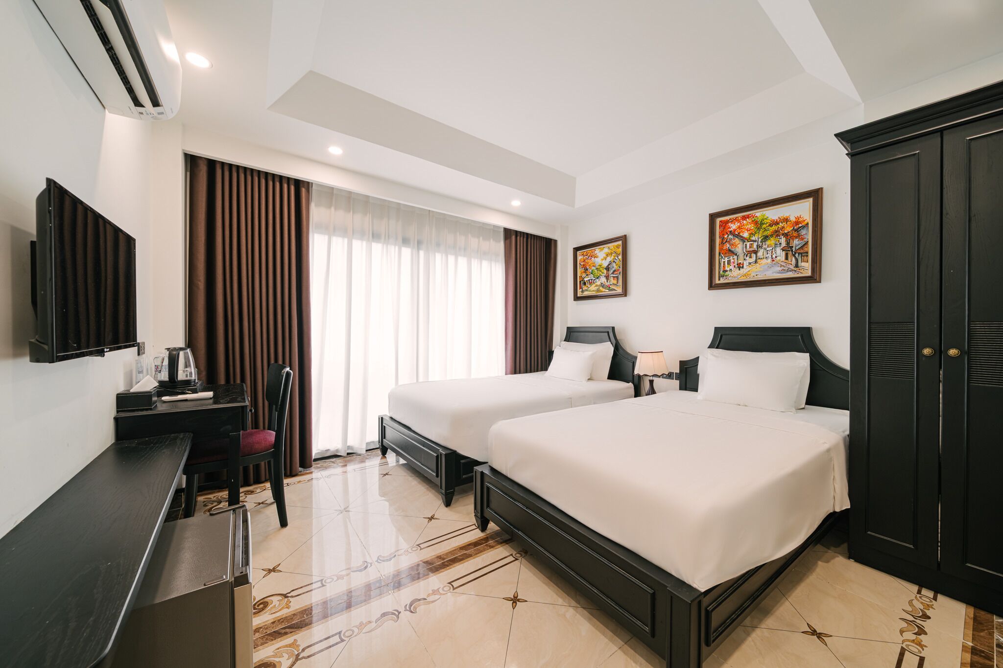 A hotel room with two beds, a desk with a chair, a television, and artwork on the walls.