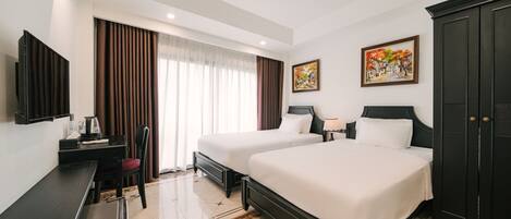 A hotel room with two beds, a desk with a chair, a television, and artwork on the walls.