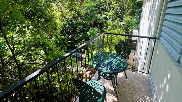 Un balcone con un tavolo rotondo e due sedie, immerso nel verde.