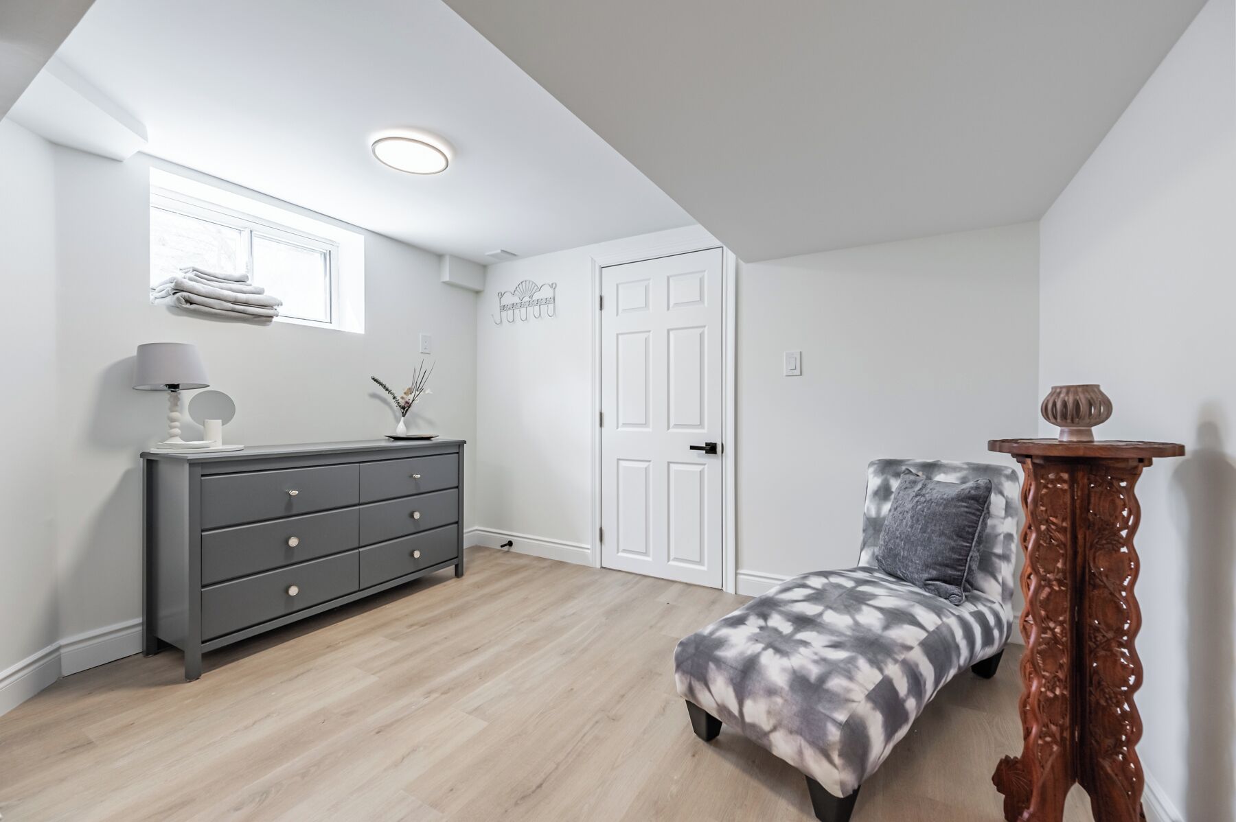 A room with a grey dresser, a chair, and a wooden side table.