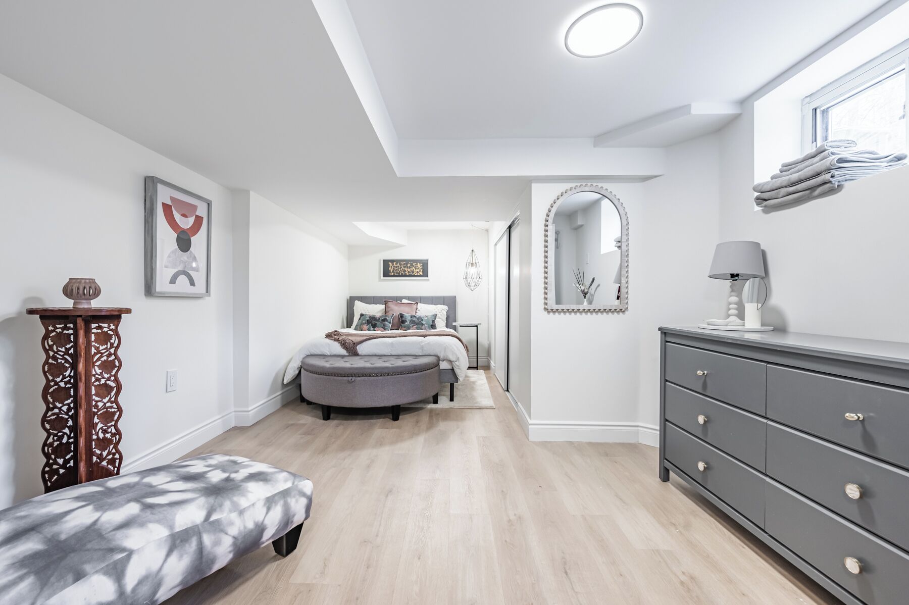A modern bedroom with a bed, bench, dresser, and a mirror.