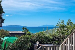 A coastal view with a clear sky, a distant mountain, and a green umbrella. - Pacific Ocean Breezes (Whangaparāoa)