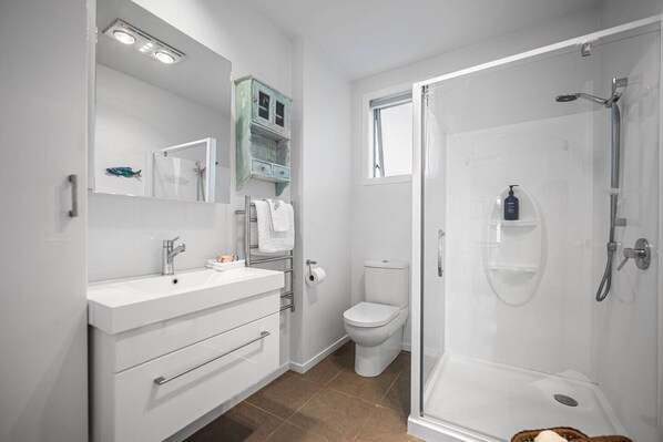 A modern bathroom with a white vanity, a glass shower enclosure, and a toilet. - Pacific Ocean Breezes (Whangaparāoa)